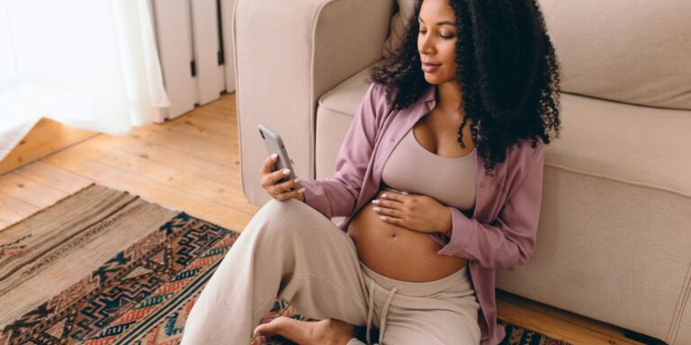 pregnant woman looking at her phone Motherly