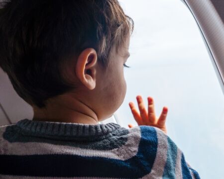 toddler boy looking out airplane window Motherly