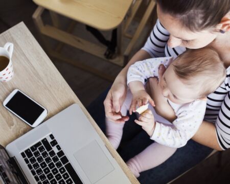 mom with baby on her lap trying to work Motherly