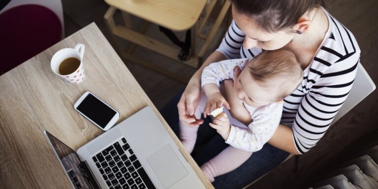 mom with baby on her lap trying to work Motherly