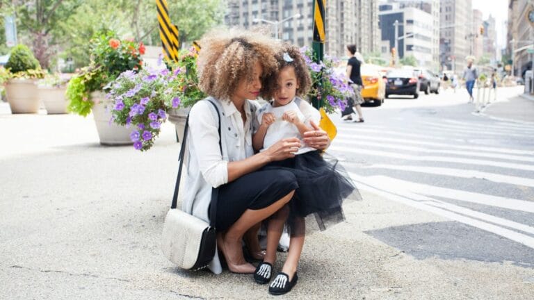 Mom kneeling with daughter on a busy city sidewalk