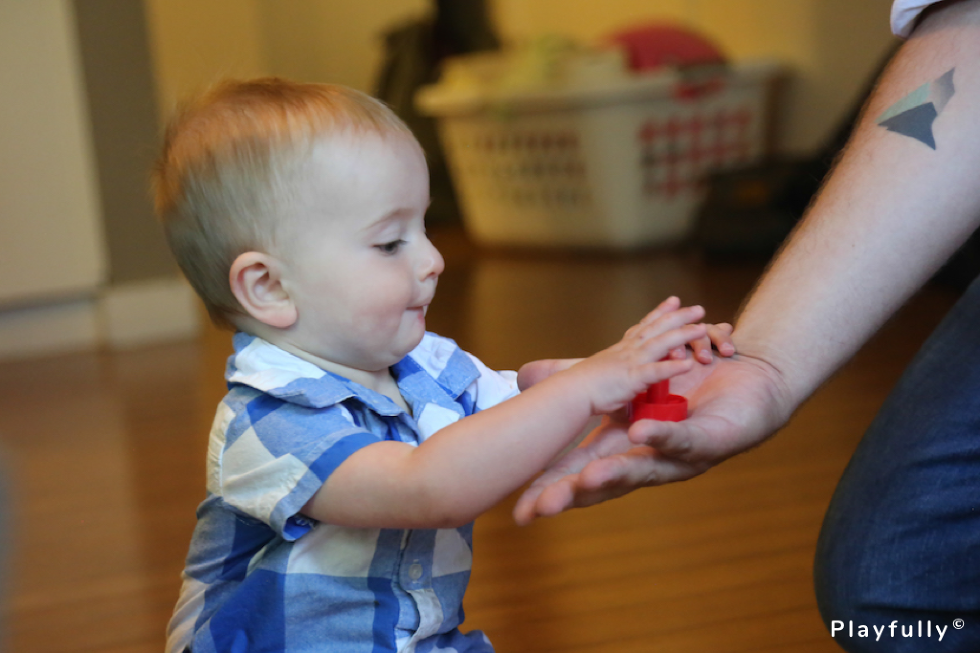 baby reaching for a red object in parent's hand