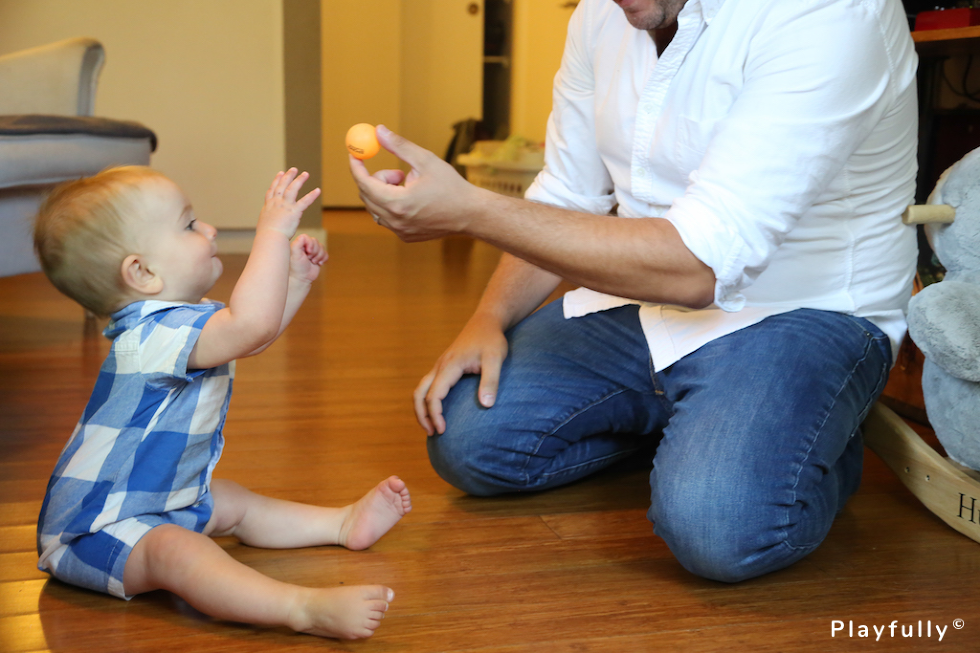 baby reaching for an orange ball in an adult's hand, stimulating baby development